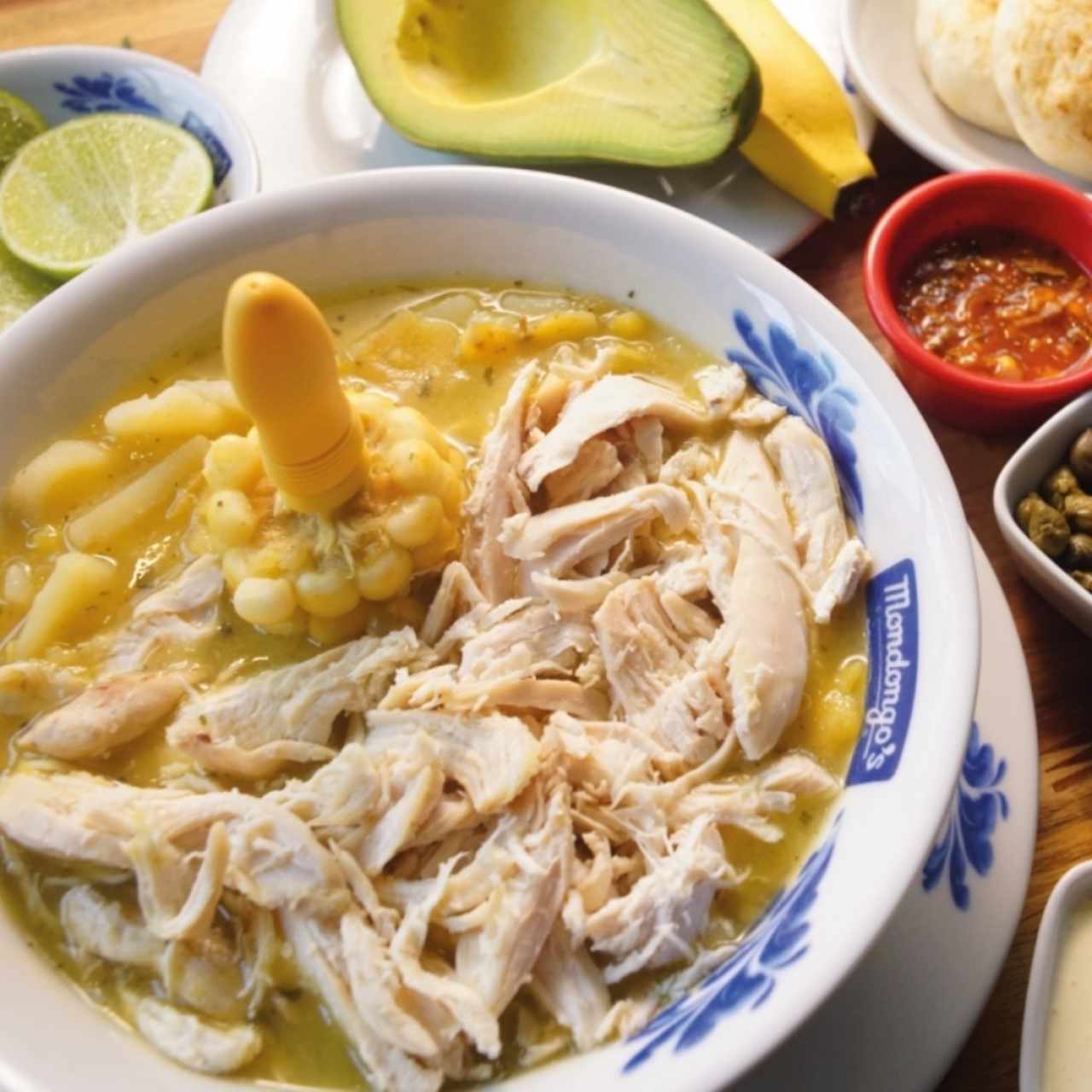 Ajiaco: papá, maíz, pollo, crema, alcaparras, cilantro, aguacate, arepa, banano y aji.