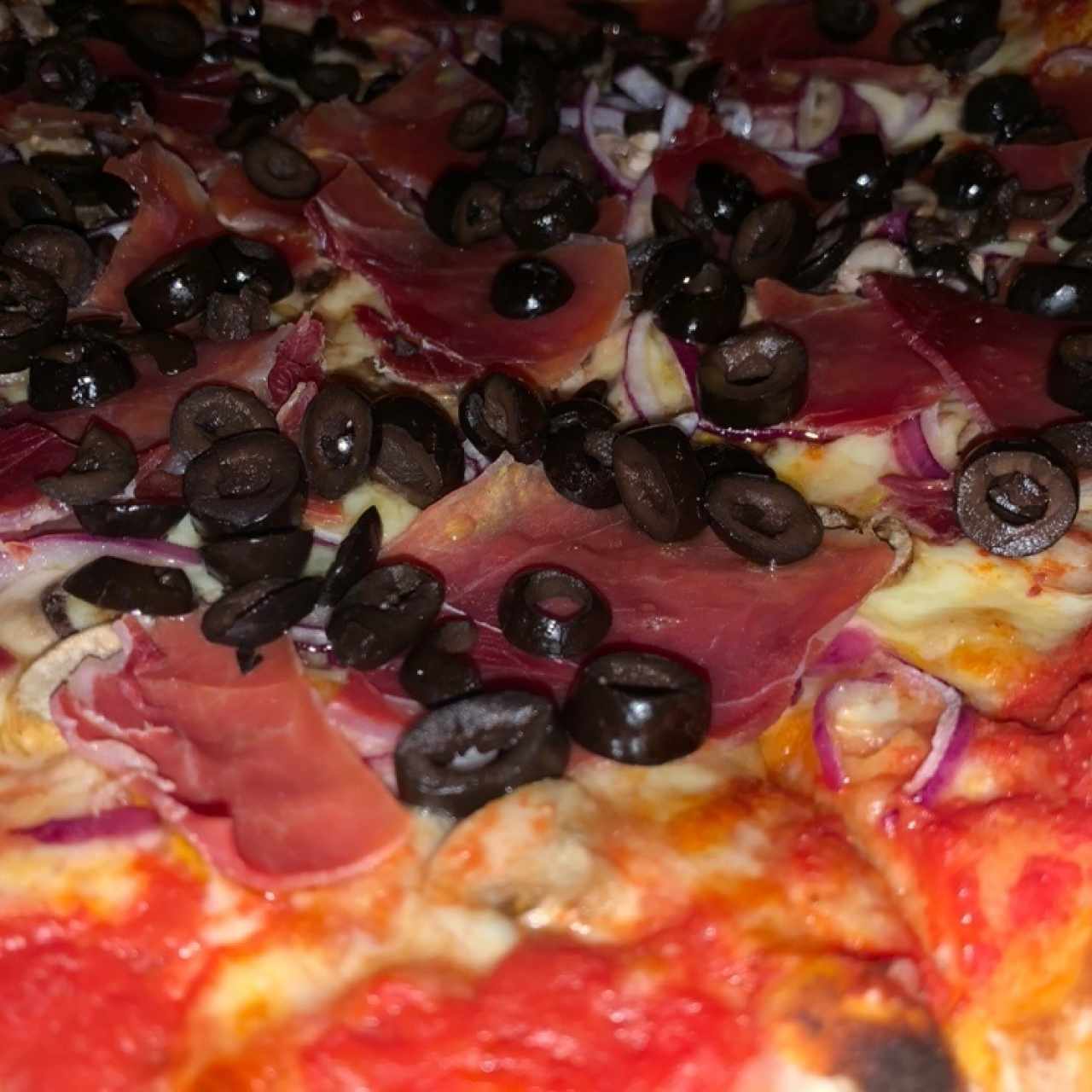 Pizza con proscuitto, aceitunas negras, hongos y cebolla morada