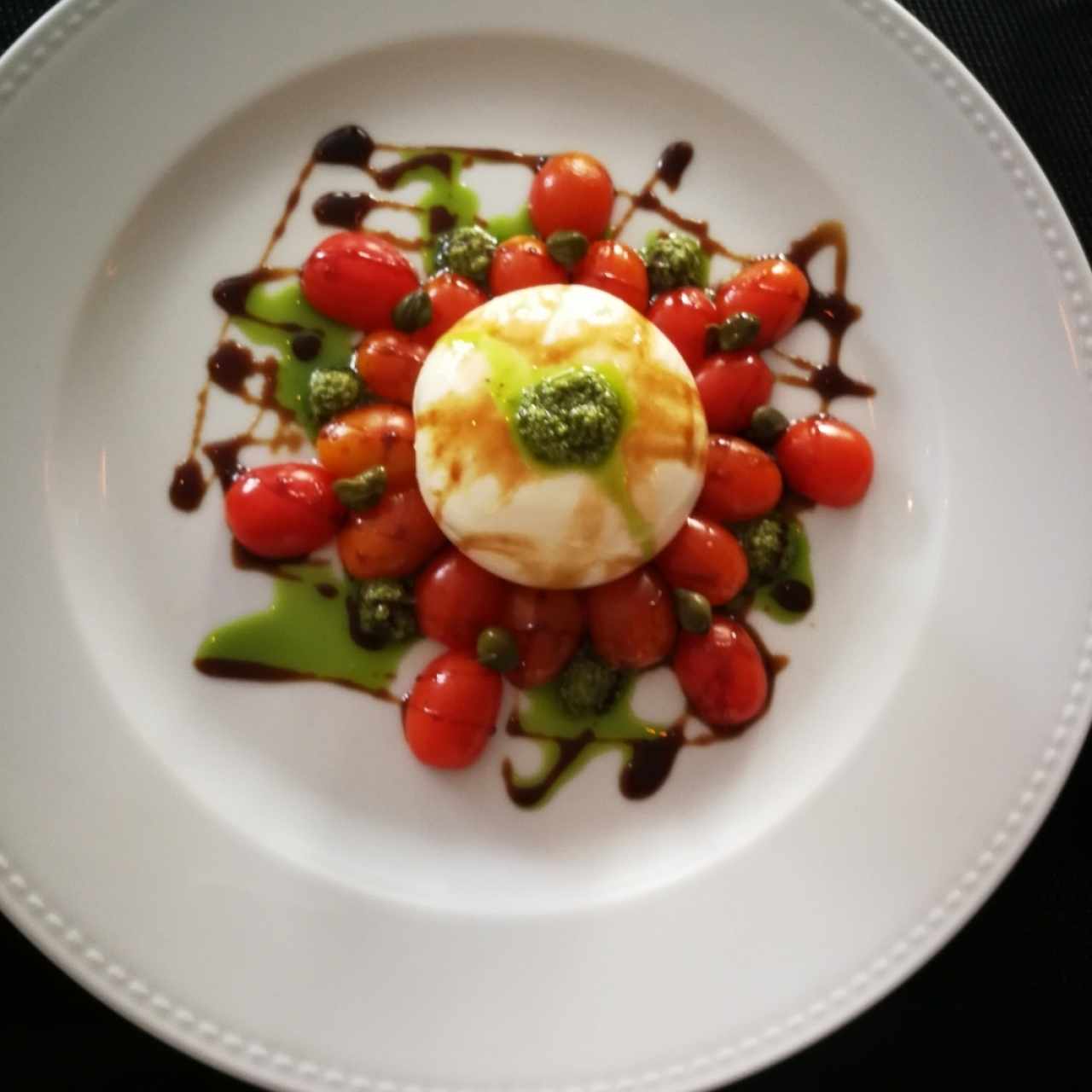 Burrata con tomate cherry, alcaparras, pesto y balsámico