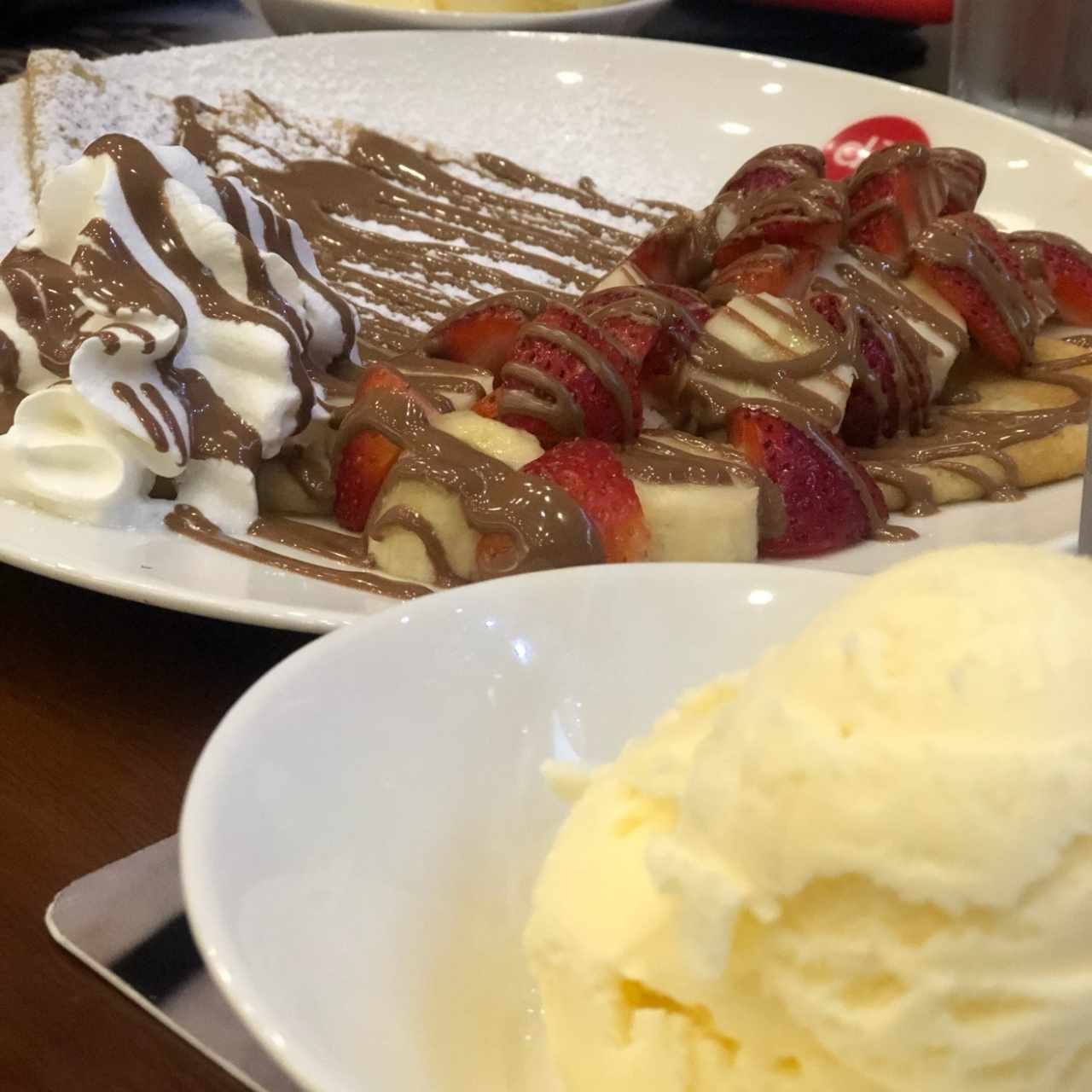 creepe con fresas y banana junto helado de vainilla