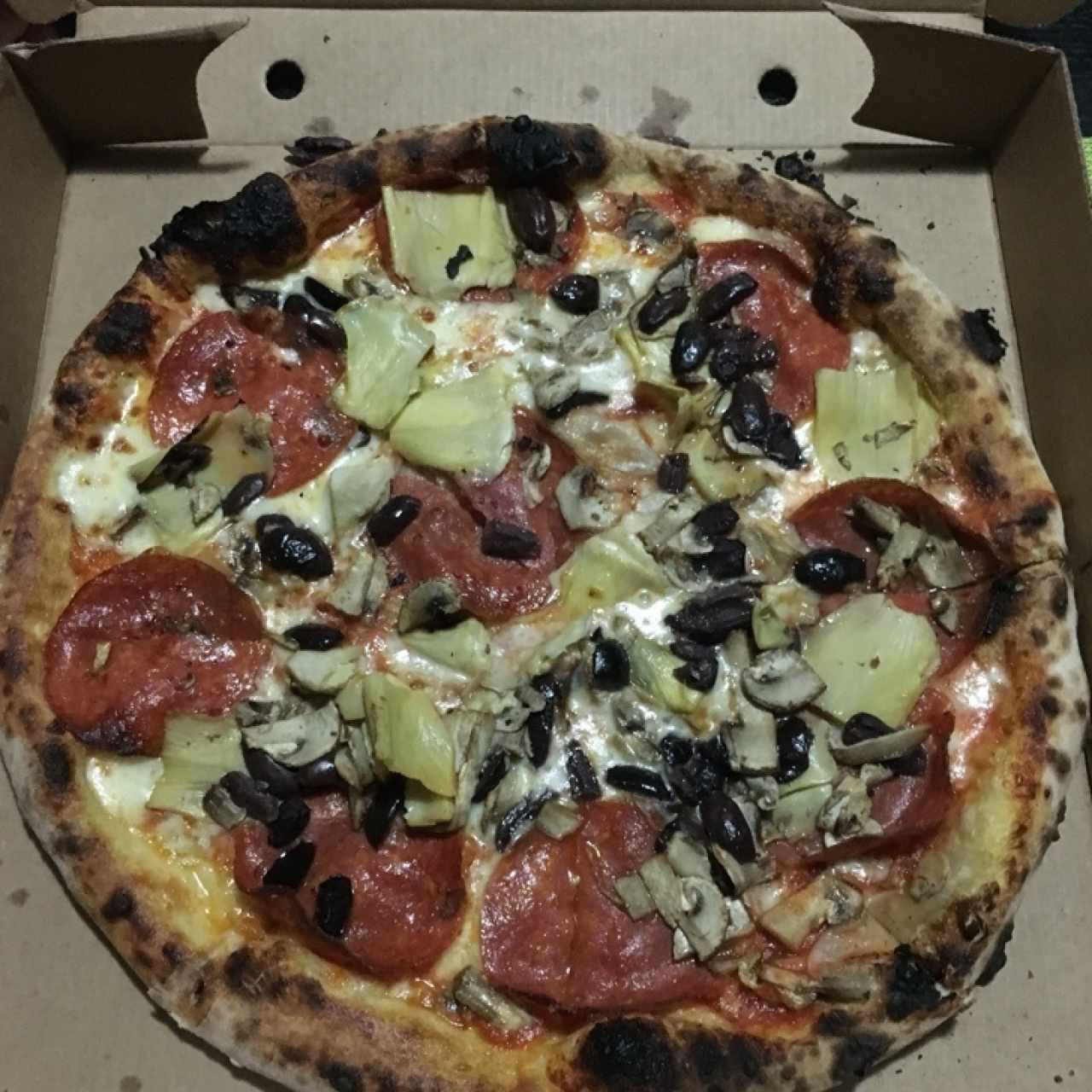 Pizza con queso mozarella, peperoni, alcachofas, aceitunas negras y hongos