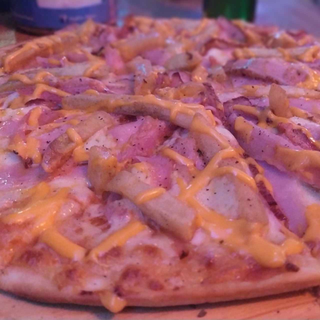 Pizza con tocineta, jamón, queso fundido y papas fritas.